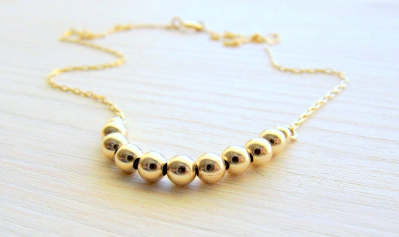 May include: A gold necklace with a chain and a row of round gold beads.