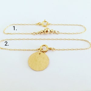 Puede incluir: Dos delicadas pulseras de oro. La primera presenta una serie de peque&ntilde;as cuentas doradas. La segunda tiene un colgante de disco dorado martillado. Ambas pulseras tienen un dise&ntilde;o de cadena simple y un cierre seguro.