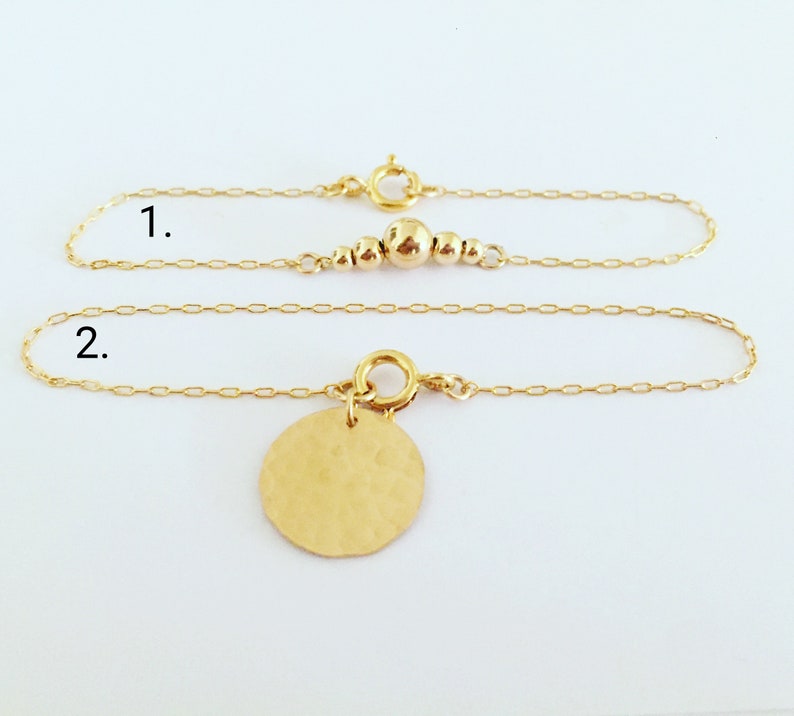 Puede incluir: Dos delicadas pulseras de oro. La primera presenta una serie de peque&ntilde;as cuentas doradas. La segunda tiene un colgante de disco dorado martillado. Ambas pulseras tienen un dise&ntilde;o de cadena simple y un cierre seguro.