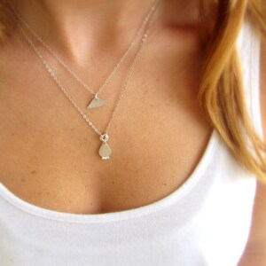 May include: A silver necklace with two pendants, one shaped like a teardrop and the other like a triangle.