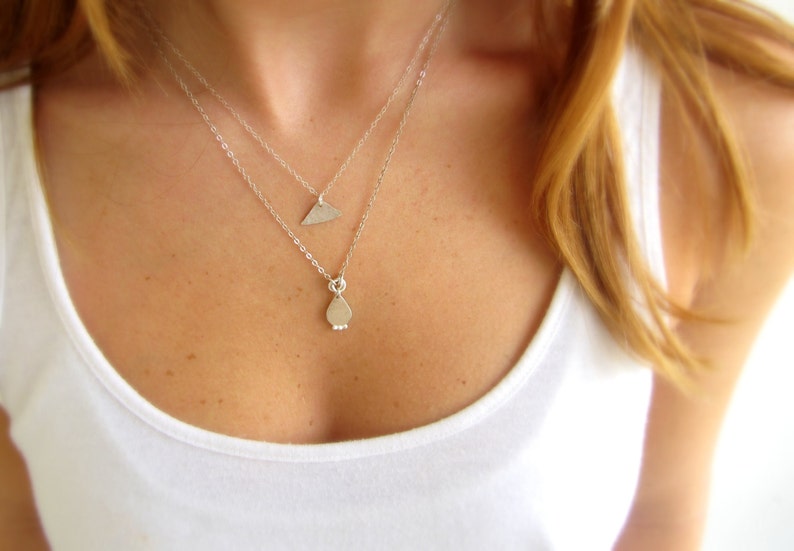 May include: A silver necklace with two pendants, one shaped like a teardrop and the other like a triangle.