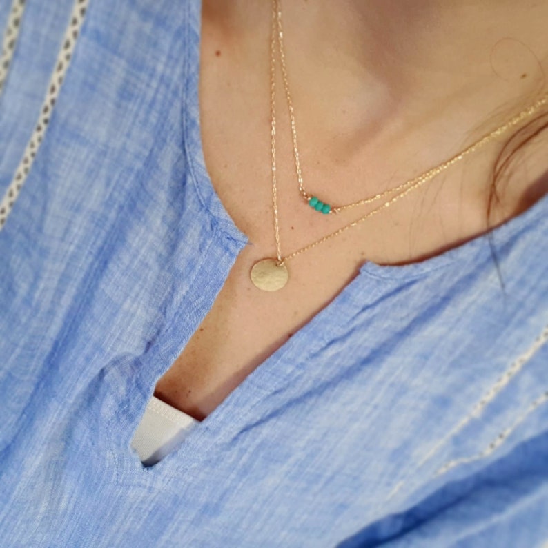 May include: A layered gold necklace with a small turquoise bead bar and a larger round pendant.
