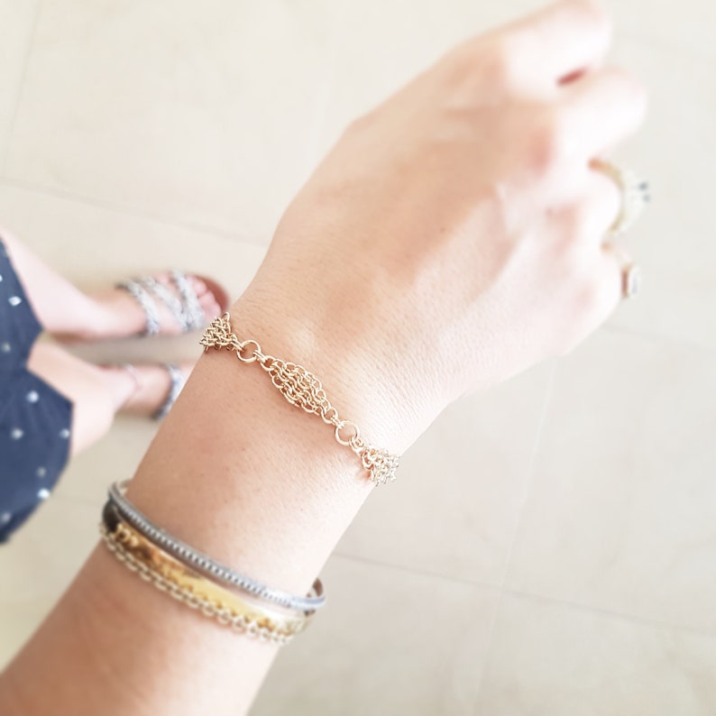 May include: A gold chain bracelet with a unique woven design. The bracelet is worn on a person's wrist with other bracelets.
