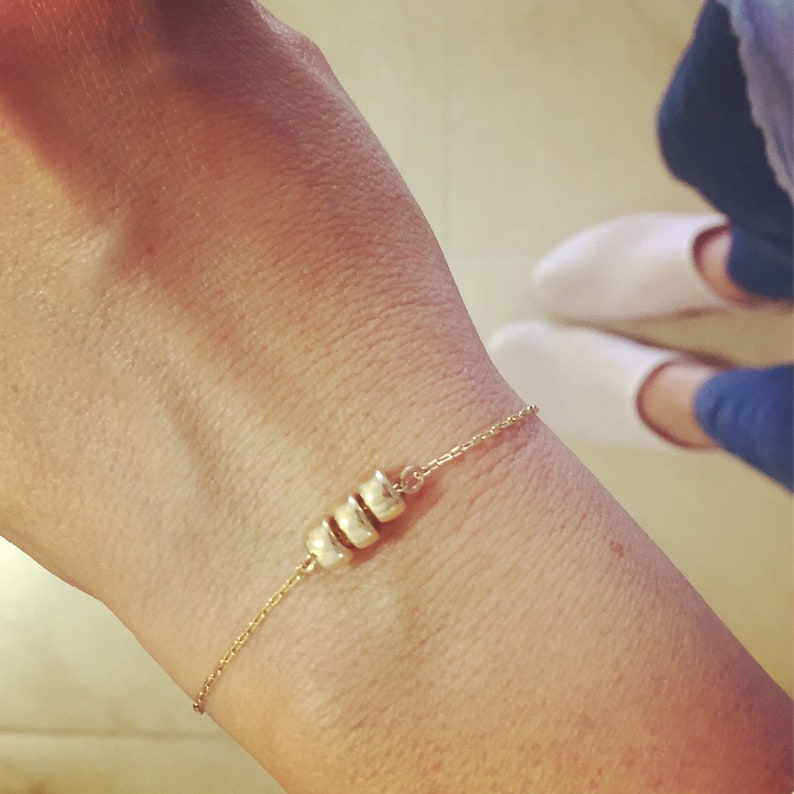 K&ouml;nnte beinhalten: Ein goldenes Kettenarmband mit einer Reihe kleiner, runder, goldener Perlen.