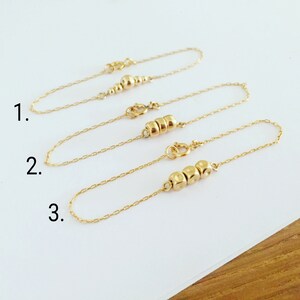 K&ouml;nnte beinhalten: Drei goldene Kettenarmb&auml;nder mit unterschiedlicher Anzahl goldener Perlen. Die Armb&auml;nder sind mit 1, 2 und 3 nummeriert.