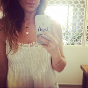 May include: A woman wearing a white lace top with a gold necklace and a gold ring. She is holding a phone with a glitter case that says "Smile" with a green and black eye design.