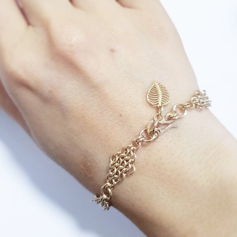 May include: A gold chain bracelet with a leaf charm. The bracelet is made of multiple chains linked together.