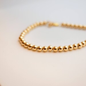 May include: A gold beaded bracelet with a simple design. The bracelet is made of small, round beads that are evenly spaced.
