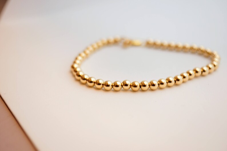 May include: A gold beaded bracelet with a simple design. The bracelet is made of small, round beads that are evenly spaced.
