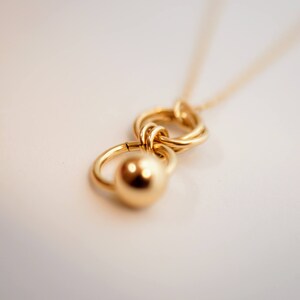 May include: A gold necklace with a pendant featuring two interlocking circles and a round ball charm.