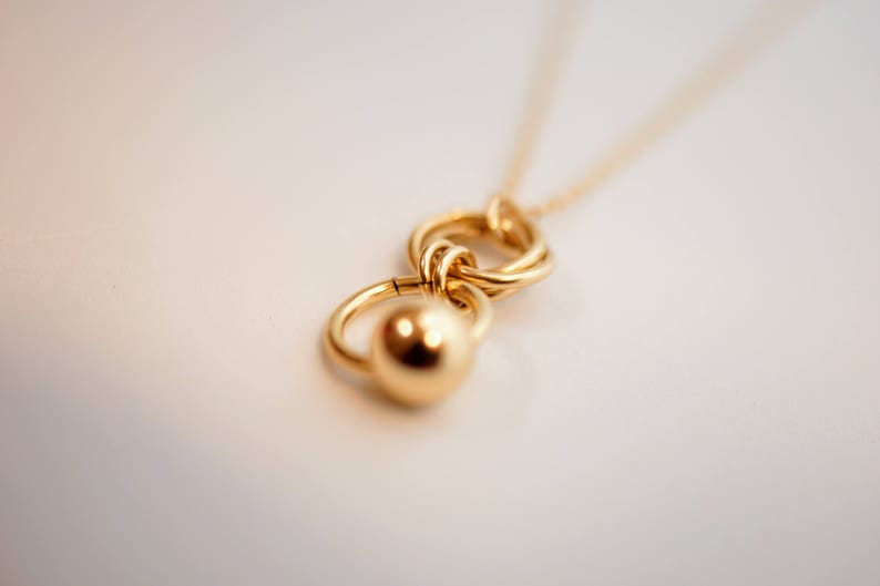 May include: A gold necklace with a pendant featuring two interlocking circles and a round ball charm.