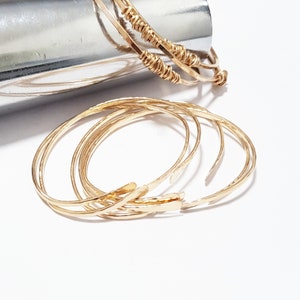 Puede incluir: Conjunto de cinco pulseras de metal martillado de color dorado. Las pulseras est&aacute;n apiladas unas sobre otras.