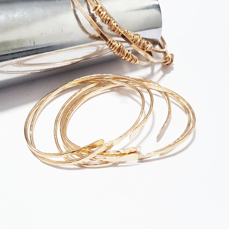 Puede incluir: Conjunto de cinco pulseras de metal martillado de color dorado. Las pulseras est&aacute;n apiladas unas sobre otras.