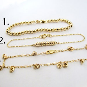 May include: Three gold bracelets with different styles. The first bracelet is a simple chain of gold beads. The second bracelet is a delicate chain with a row of small gold rings. The third bracelet is a chain with small gold rings and a few dangling gold rings.