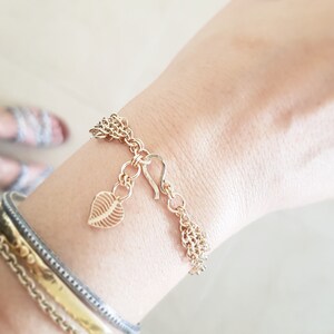 May include: A gold chain bracelet with a leaf charm and a hook clasp. The bracelet is layered and has a delicate design.