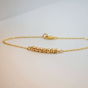 Puede incluir: Un brazalete de cadena dorada con una fila de peque&ntilde;as cuentas redondas.