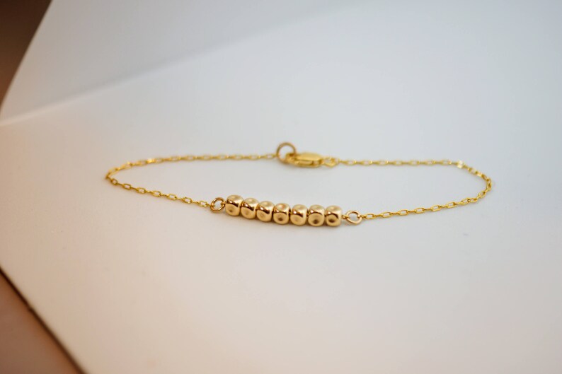 Puede incluir: Un brazalete de cadena dorada con una fila de peque&ntilde;as cuentas redondas.