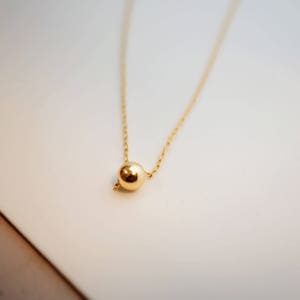 May include: A delicate gold chain necklace with a single, round gold pendant.