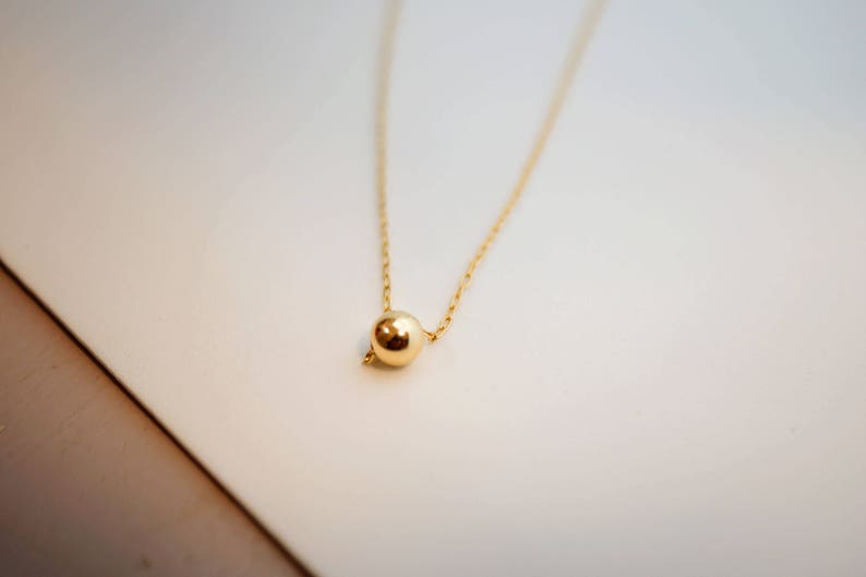 May include: A delicate gold chain necklace with a single, round gold pendant.