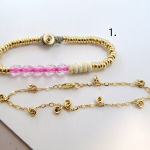 May include: Two bracelets. The top bracelet features gold beads, pink crystal beads, and off-white beads. The bottom bracelet is a delicate gold chain with small, spiral-shaped gold accents. Both bracelets are displayed on a white surface.