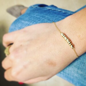 May include: A gold bracelet with a chain and a long, thin charm made of stacked gold rings.