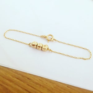 K&ouml;nnte beinhalten: Ein zartes Armband aus goldener Kette mit drei kleinen, runden, strukturierten Perlen.