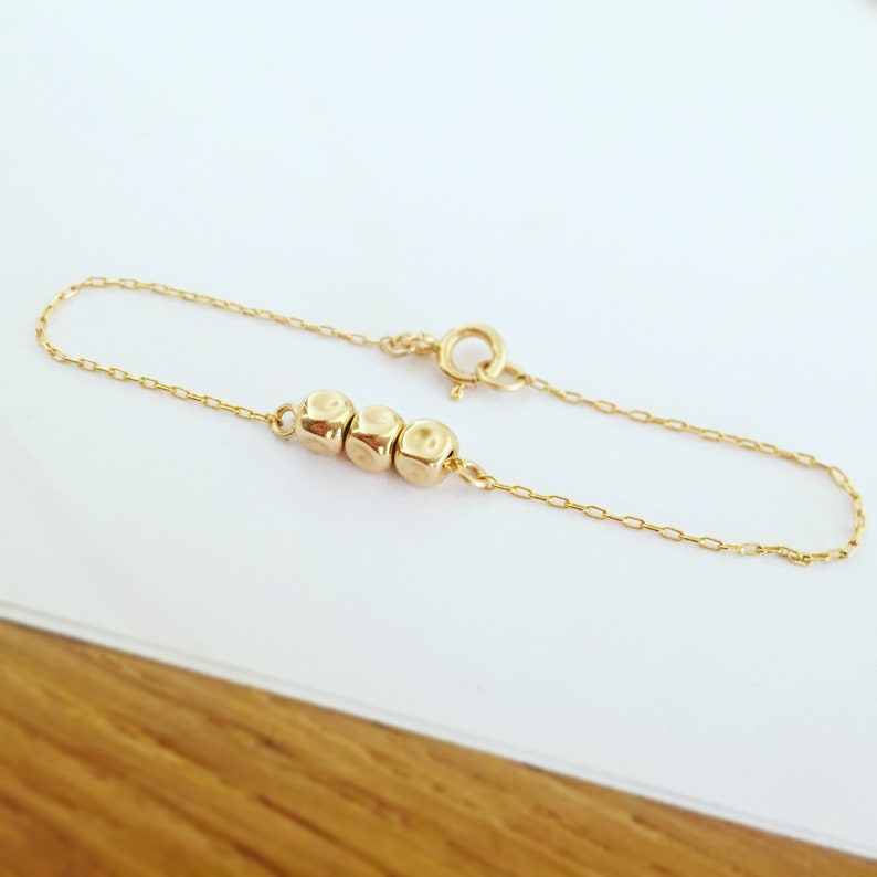 K&ouml;nnte beinhalten: Ein zartes Armband aus goldener Kette mit drei kleinen, runden, strukturierten Perlen.