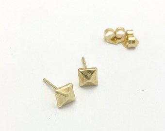 May include: A pair of gold pyramid-shaped stud earrings. The earrings are small and have a simple design.