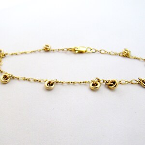 May include: A gold chain bracelet with multiple small gold circles hanging from it.