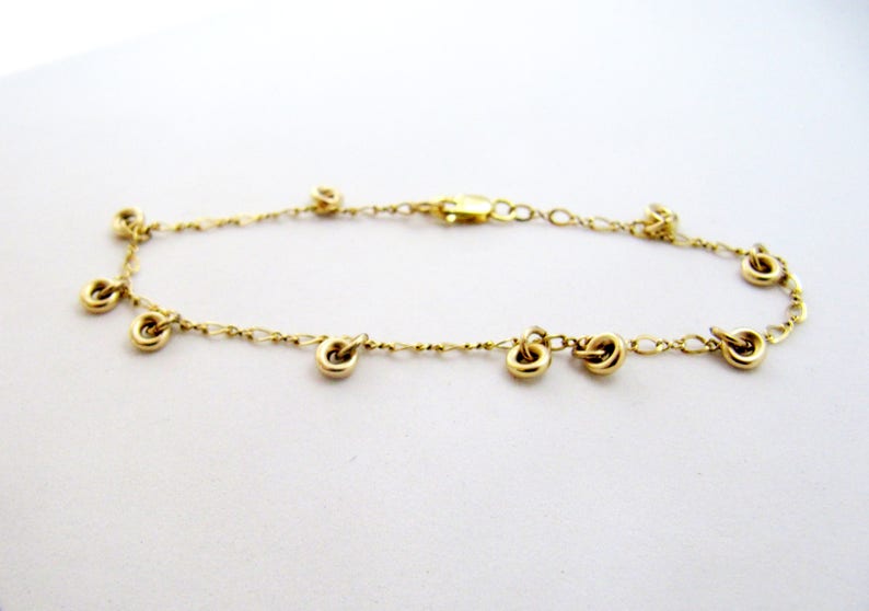 May include: A gold chain bracelet with multiple small gold circles hanging from it.