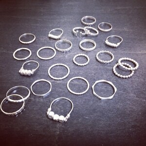 May include: A collection of silver rings, some with textured designs, others with simple bands. The rings are arranged on a dark surface.