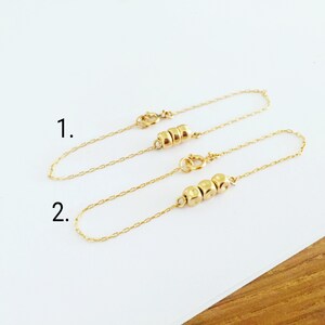 Pu&ograve; includere: Due braccialetti a catena d'oro con piccole perle d'oro. Il braccialetto superiore ha tre perle e quello inferiore ne ha quattro. I braccialetti sono numerati 1 e 2.