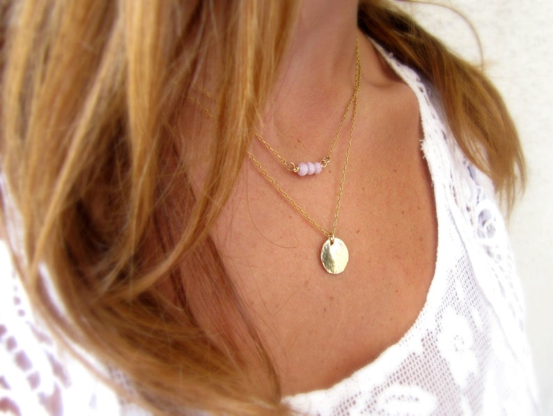 May include: A layered gold necklace with a small circle pendant and a delicate chain with tiny pink beads.