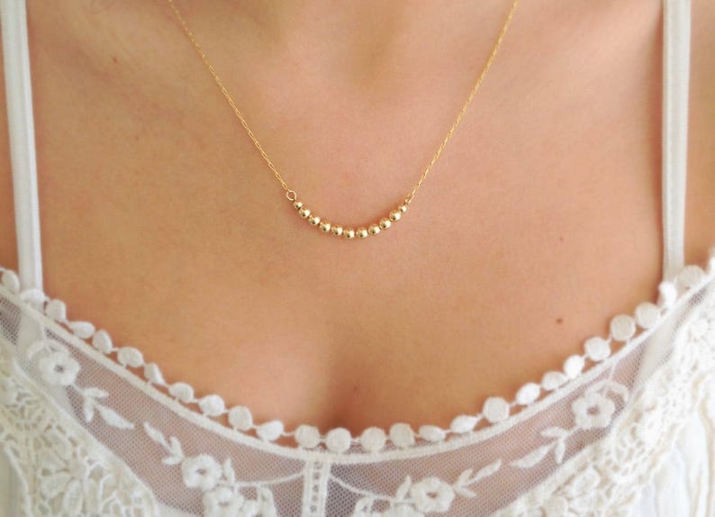 May include: A gold necklace with a delicate chain and a row of small, round beads.