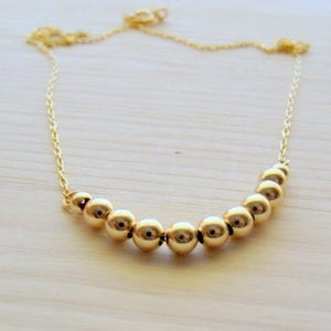 May include: A gold necklace with a curved row of round gold beads.
