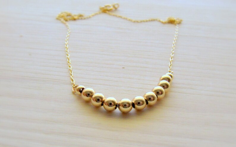 May include: A gold necklace with a curved row of round gold beads.