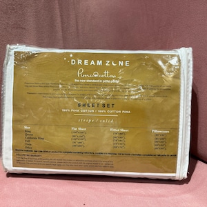 May include: A packaged sheet set with the text "DREAM ZONE Pima Cotton" in gold lettering. The packaging lists sizes for King, Queen, California King, Full, Twin, and other. The sheet set is made of 100% Pima cotton.