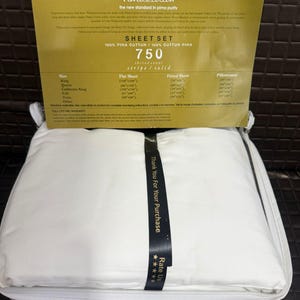 May include: A white sheet set in a zippered case, with a gold-colored label on top. The label reads "Wamsutta Dream Zone Pima Cotton" and "Sheet Set 750 thread count stripe/solid." A black ribbon with "Thank You For Your Purchase" is wrapped around the sheets.