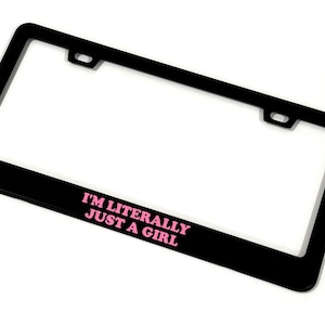 May include: Black license plate frame with the text "I'M LITERALLY JUST A GIRL" in pink. The frame has a rectangular shape with rounded corners and mounting holes. The background is white.