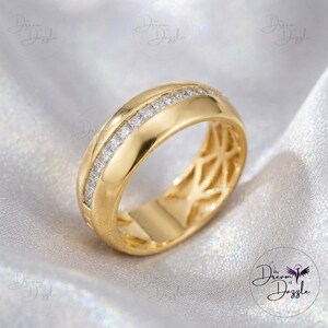 May include: A gold band ring featuring a central channel set with a row of small, clear, square-cut stones. The ring has a polished, smooth finish on the outer edges and a hollowed-out, intricate lattice pattern visible on the inner band surface.