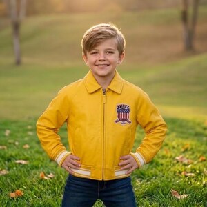 May include: A yellow leather jacket with a zipper closure and a patch on the chest. The jacket has white and light blue striped cuffs and a white stripe at the bottom. The jacket is paired with blue jeans.