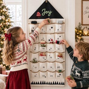Può includere: Un calendario dell'avvento in tessuto da appendere con una parte superiore triangolare nera che riporta la scritta Joy e un disegno di fungo rosso. Il corpo rettangolare bianco ha ventiquattro tasche numerate con icone nere e una stampa a montagne.