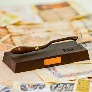 May include: A wooden display stand with a miniature broom, featuring the text "Anna" and "Nimbus 2000". The broom is brown with gold accents. The stand is dark brown and rectangular.