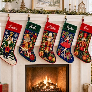 Pode incluir: Cinco meias de Natal penduradas em fila, cada uma com um design bordado único, incluindo um quebra-nozes, um rato, um soldado e uma bailarina. As meias têm punhos de veludo vermelho ou verde com os nomes Lucia, Perla, Alisha, Sophia e Evi bordados em letra branca. Cada meia exibe motivos festivos como flocos de neve, ornamentos e folhagens.