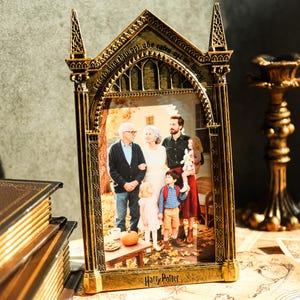 Puede incluir: Un marco de fotos dorado de estilo gótico con las palabras "Harry Potter" en la parte inferior. El marco contiene un retrato familiar. El marco tiene detalles intrincados y un diseño de arco apuntado.