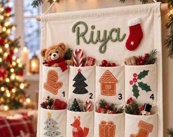 Puede incluir: Un calendario de Adviento de tela color crema colgado de una varilla de madera, con el nombre Riya en hilo verde, un calcetín rojo y ocho bolsillos numerados del 1 al 8. Cada bolsillo muestra iconos festivos como una manopla, árboles, una casa de jengibre, un zorro, un regalo y un calcetín, rellenos con pequeños adornos navideños.