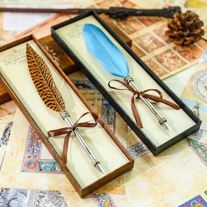 May include: Two feather quill pens in decorative boxes. One pen has a brown and black striped feather, the other a blue feather. Both pens have silver-colored metal barrels and are tied with brown ribbons. The boxes are brown and black, and the background is a vintage map.