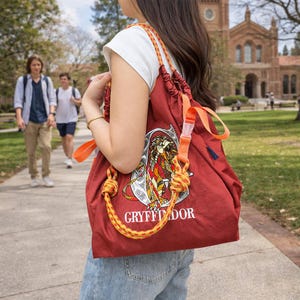Peut inclure: Un sac à dos à cordon de couleur marron orné d'un grand écusson brodé représentant le lion de Gryffondor et le texte Gryffindor en blanc. Le sac possède des cordes épaisses nouées jaune et orange et une sangle en nylon orange avec boucle.