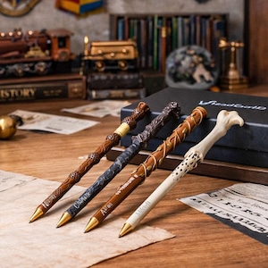 May include: Four decorative pens with gold tips, each featuring unique designs. The pens are brown, gray, and white, with intricate detailing. One pen has the name "Aaron" on it. The pens are displayed on a wooden surface.