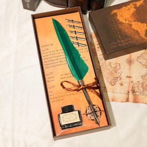 May include: A vintage calligraphy set in a decorative box. The set includes a green feather quill pen, ink bottle, and several nibs. The box has a printed paper with text and a compass rose design. A second box with a world map is also visible.